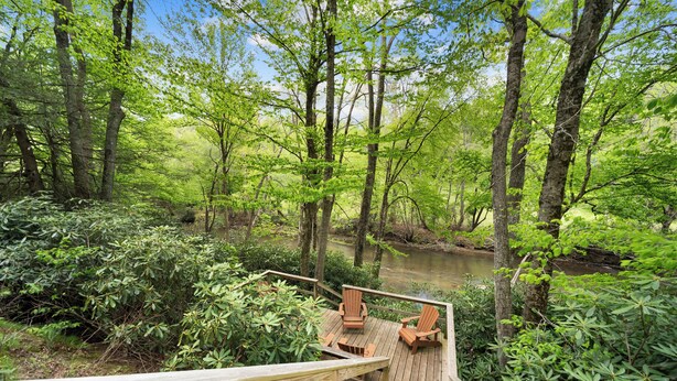 A wooden deck with chairs overlooking a river in a forest.