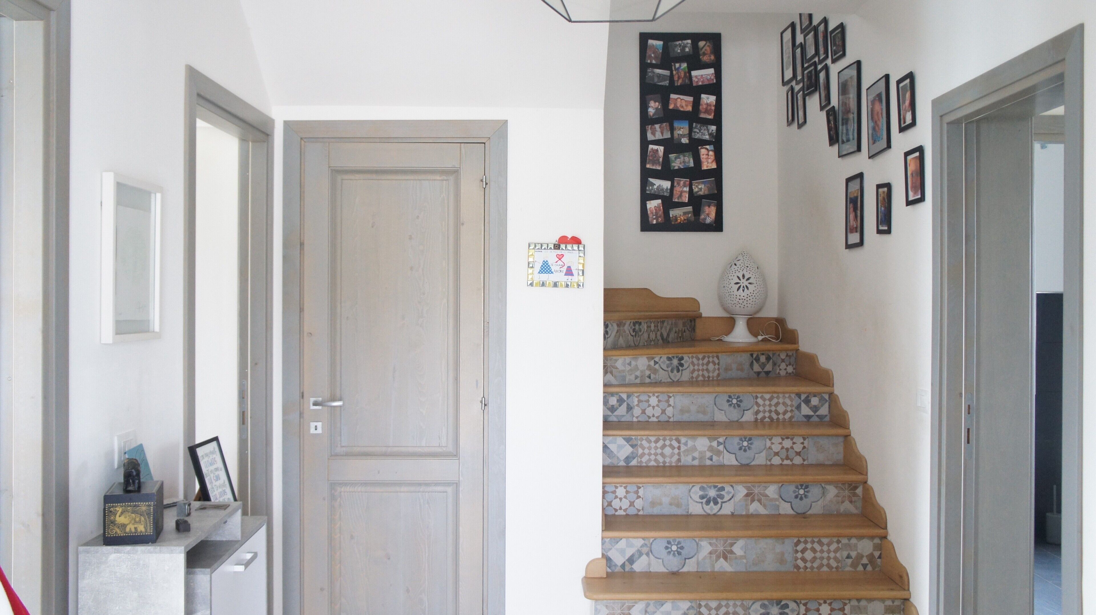 A staircase with patterned tiles, a door with a heart-shaped sign, and a wall with multiple framed photos.