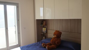 Et soveværelse med en seng, et vindue, en bamse og en reol.
