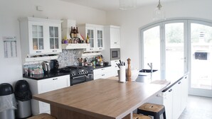 Uma cozinha moderna com armários brancos, uma ilha de madeira e vista através de uma porta de vidro.