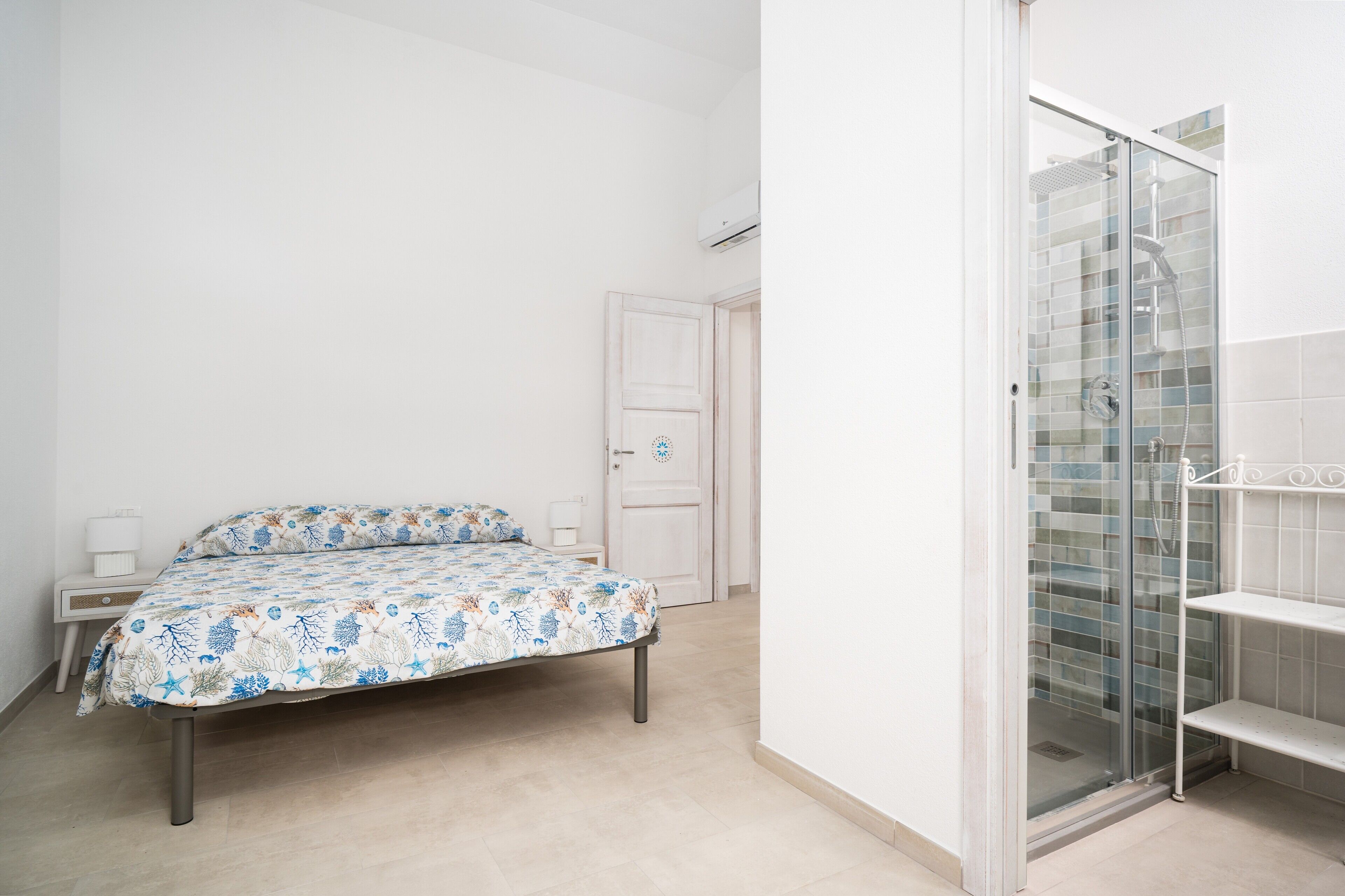 Un dormitorio con cama, mesita de noche, puerta y zona de ducha con puerta de cristal.