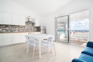 A modern kitchen with white cabinets, a tiled backsplash, and a view of the sea through a glass door. - Holiday Home 'Girasole' with Sea View, Private Terrace & Air Conditioning (La Caletta)