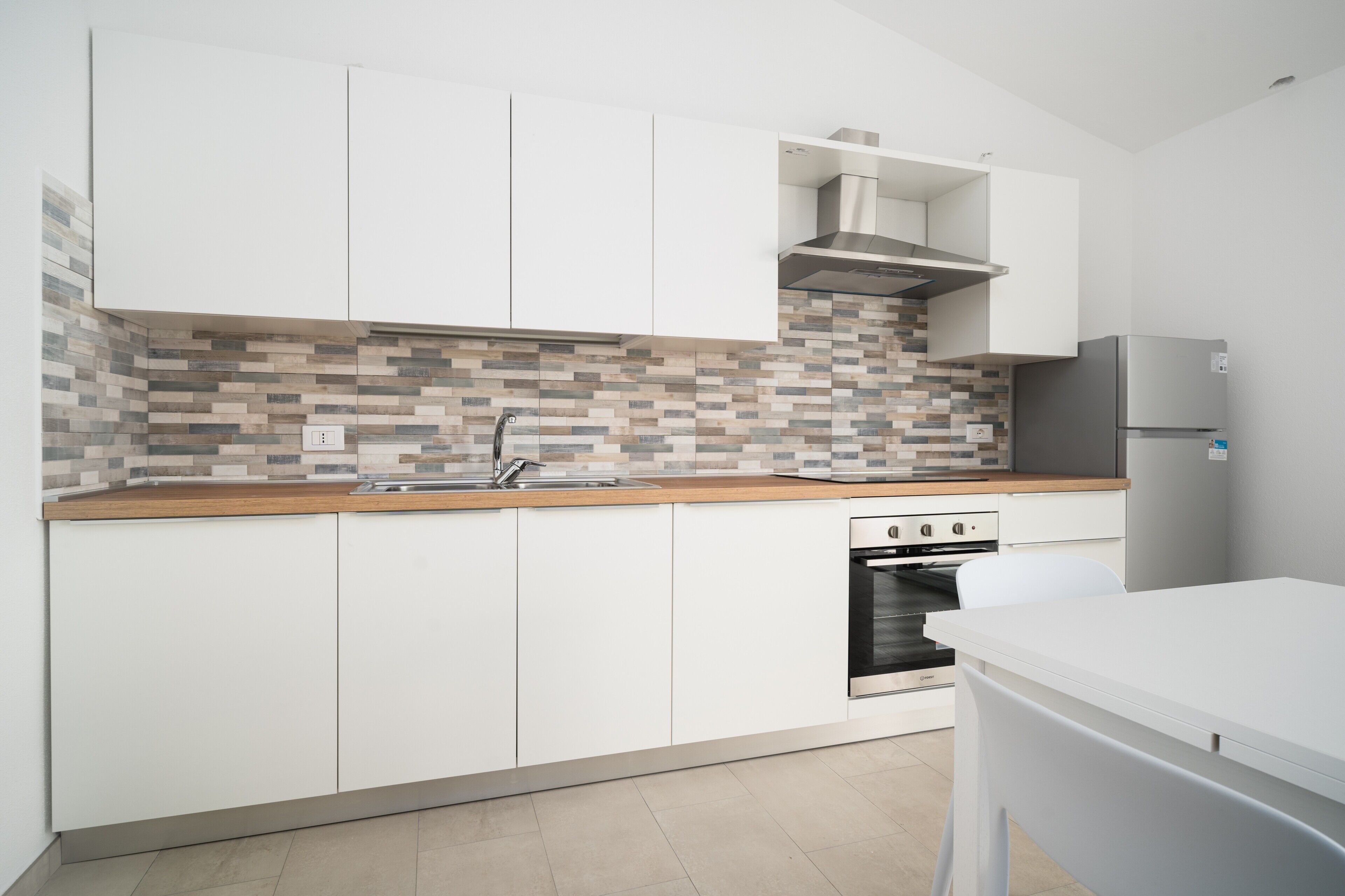 A modern kitchen with white cabinets, a tiled backsplash, a stainless steel range hood, and a built-in oven.