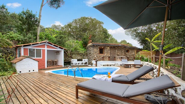 Um deck de madeira com piscina, espreguiçadeiras e um pequeno edifício com telhado vermelho.