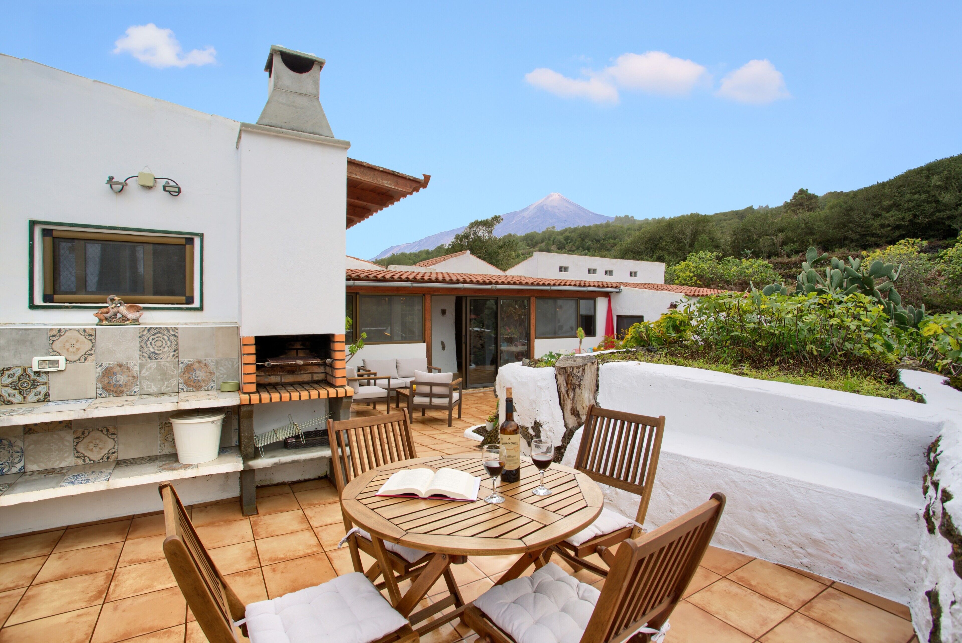 Un patio con una mesa redonda de madera, sillas y una parrilla.