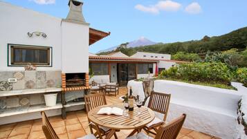 Un patio con una mesa redonda de madera, sillas y una parrilla.