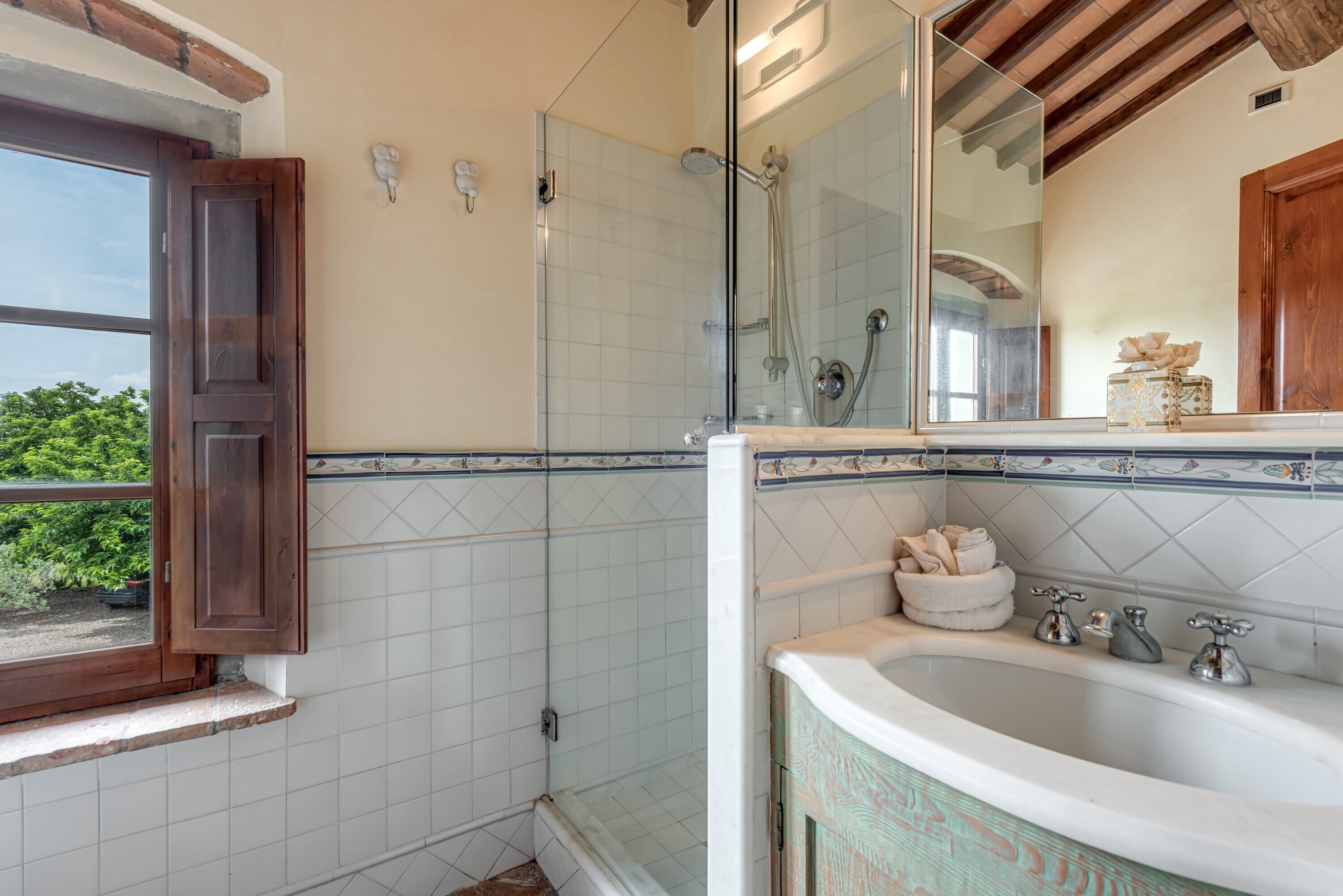 A bathroom with a shower, a sink with a mirror, and a window with a wooden frame.