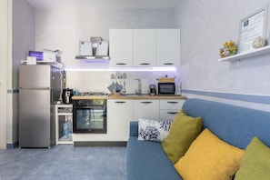 A compact kitchen with a refrigerator, oven, microwave, and a small dining area. - Apartment 'D R Holiday Home' with Private Garden close to the sea (Santa Maria del Focallo)