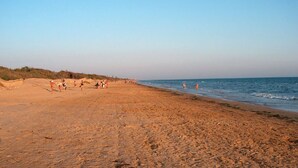 Ein weiter, sandiger Strand mit Menschen, die laufen und stehen, und ein klarer Himmel.
