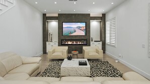 Una sala de estar moderna con chimenea, un televisor de pantalla plana grande y dos sofás color beige.