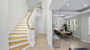 Un interior espacioso con una escalera de madera, zona de comedor y ventanas amplias.