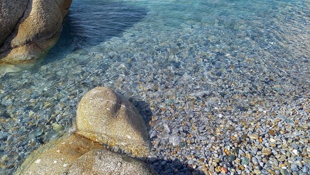 Ein freier Blick auf einen Kiesstrand mit großen Felsen und ruhigem Wasser.