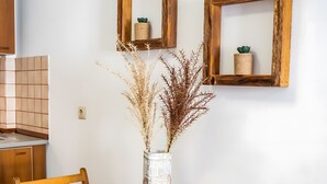 A wooden dining table with woven placemats, a vase with dried plants, and two wooden-framed mirrors on the wall. - Apartment '1' with Mountain View, Wi-Fi and Air Conditioning (Karpathos Town)