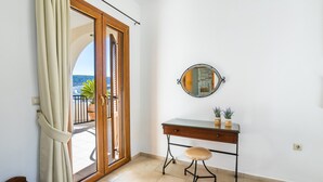 A room with a sliding glass door leading to a balcony, a desk with a mirror, and a small stool. - Apartment '1' with Mountain View, Wi-Fi and Air Conditioning (Karpathos Town)