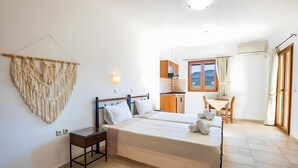 A bedroom with two beds, a bedside table, a wall-mounted macrame piece, a window with curtains, and a view of the sea. - Studio Apartment 'No 2' with Mountain View, Wi-Fi and Air Conditioning (Karpathos Town)