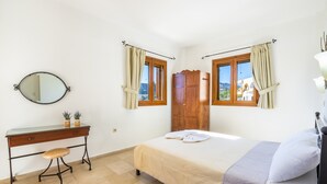 A bedroom with a bed, a wooden wardrobe, a desk with a chair, a mirror, and two windows with curtains. - Apartment '2' with Mountain View, Wi-Fi and Air Conditioning (Karpathos Town)