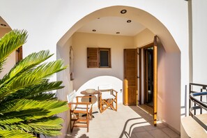 Eine sonnendurchflutete Terrasse mit Tisch und Stühlen, einer Holztür und einer Palme.