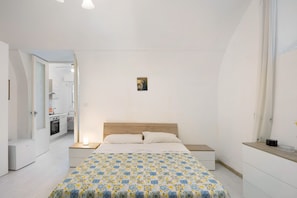 A bedroom with a bed, bedside tables, a nightstand, a small bedside lamp, a wooden headboard, and a wall-mounted picture.