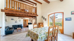 A dining area with a table set for four, a wooden staircase, a living room with a sofa and chairs, and a view through a glass door. - Holiday Home 'La Provençale' with Private Pool, Private Terrace and Wi-Fi (Châteaurenard)
