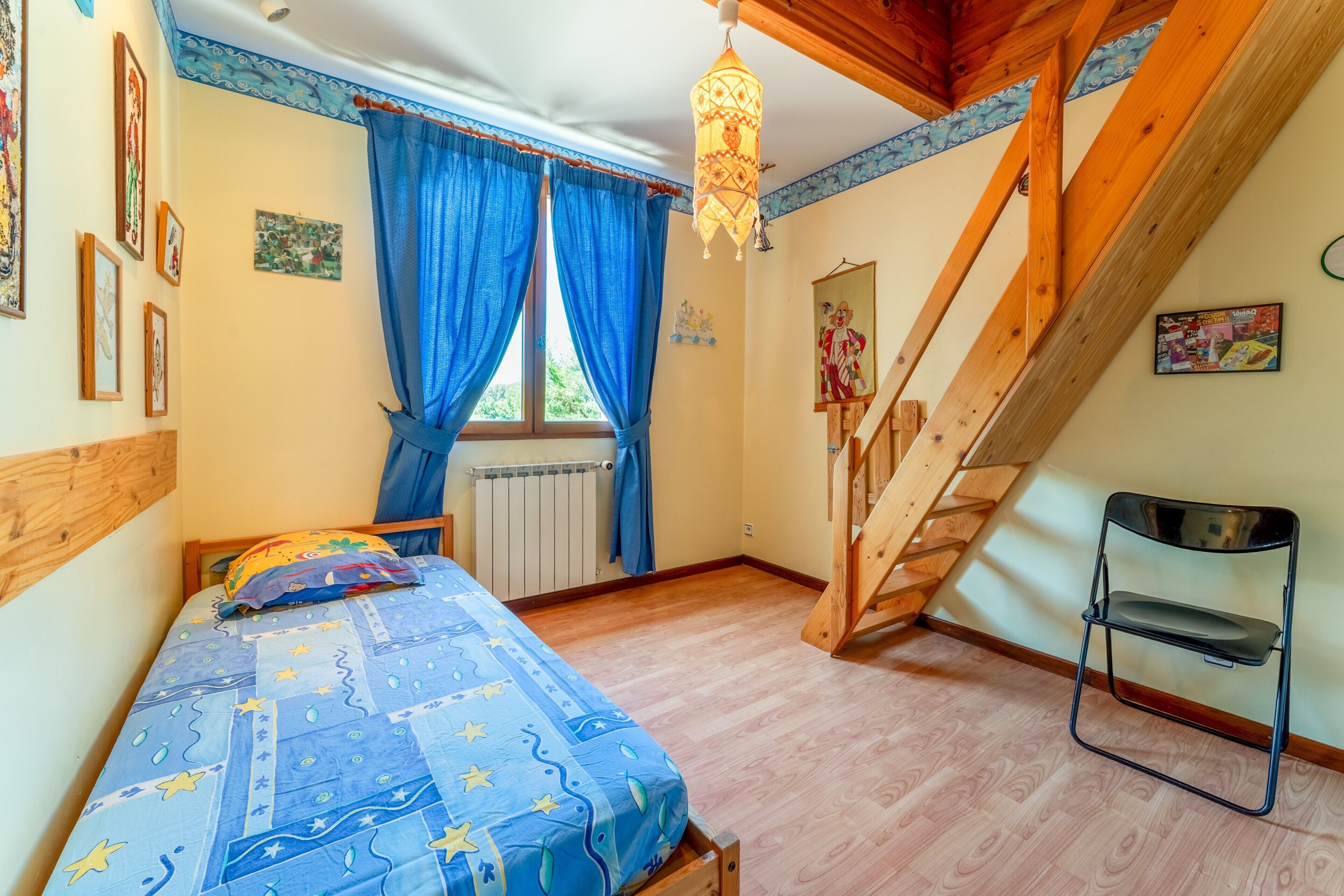 Une chambre à coucher comprenant un lit, une chaise, une fenêtre avec des rideaux, un radiateur et un escalier en bois.
