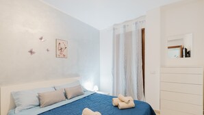 A bedroom with a bed, pillows, a bedside table, a mirror, and a wardrobe.