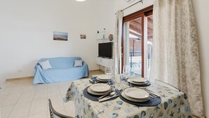 A dining area with a table set for four, a blue sofa, a television, and a view through a glass door.
