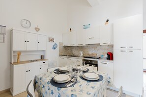 Une cuisine avec des meubles blancs, une table à manger dressée pour quatre personnes et une horloge au mur.