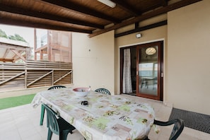 Une terrasse extérieure avec une table dressée pour les repas, entourée de chaises, et une zone de pont en bois.