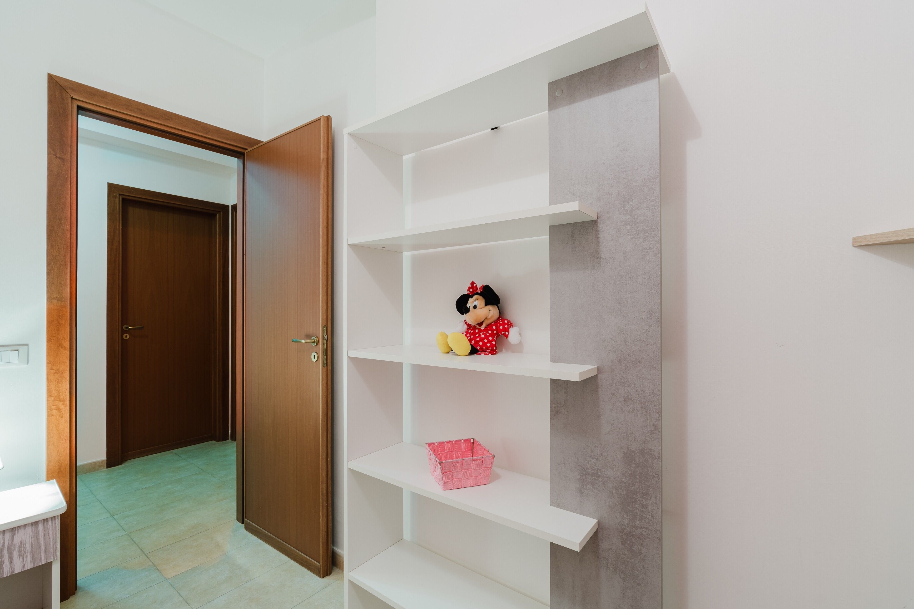 A room with a wooden door, white shelving unit, and a pink basket.