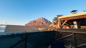A mountainous landscape with a clear sky, a building with a wooden deck, and a view of a bridge in the distance.