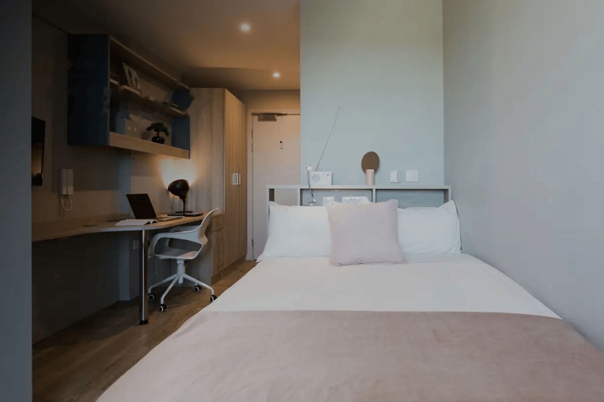 A bedroom with a bed, a desk, and a chair.