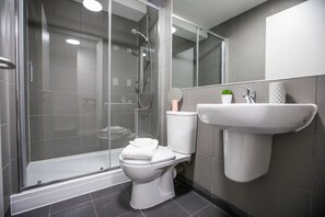 A modern bathroom with a glass-enclosed shower, a toilet, and a sink.