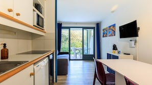 A compact kitchen with a dishwasher, microwave, and a dining area with a table and chairs. - Cozy Studio in Moliets et Maa with Private Terrace, Barbecue, Ideal for 4 Guests (Moliets et maa)