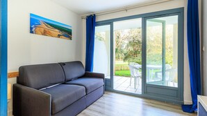 A room with a grey sofa, a painting on the wall, and a sliding glass door leading to an outdoor area with a table and chairs. - Cozy Studio in Moliets et Maa with Private Terrace, Barbecue, Ideal for 4 Guests (Moliets et maa)