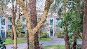 A tree-lined courtyard with bicycles parked, a building with blue and red exterior, and a clear sky. - Cozy Studio in Moliets et Maa with Private Terrace, Barbecue, Ideal for 4 Guests (Moliets et maa)