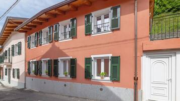 Un edificio de varios pisos con contraventanas verdes, puertas blancas y plantas en macetas en los alféizares.
