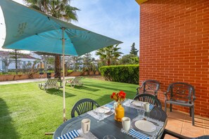 Um pátio com uma mesa posta para refeições, rodeado por cadeiras e um guarda-sol.