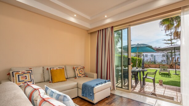 Una sala de estar con sofá, reposapiés y vistas a un patio con mobiliario exterior.