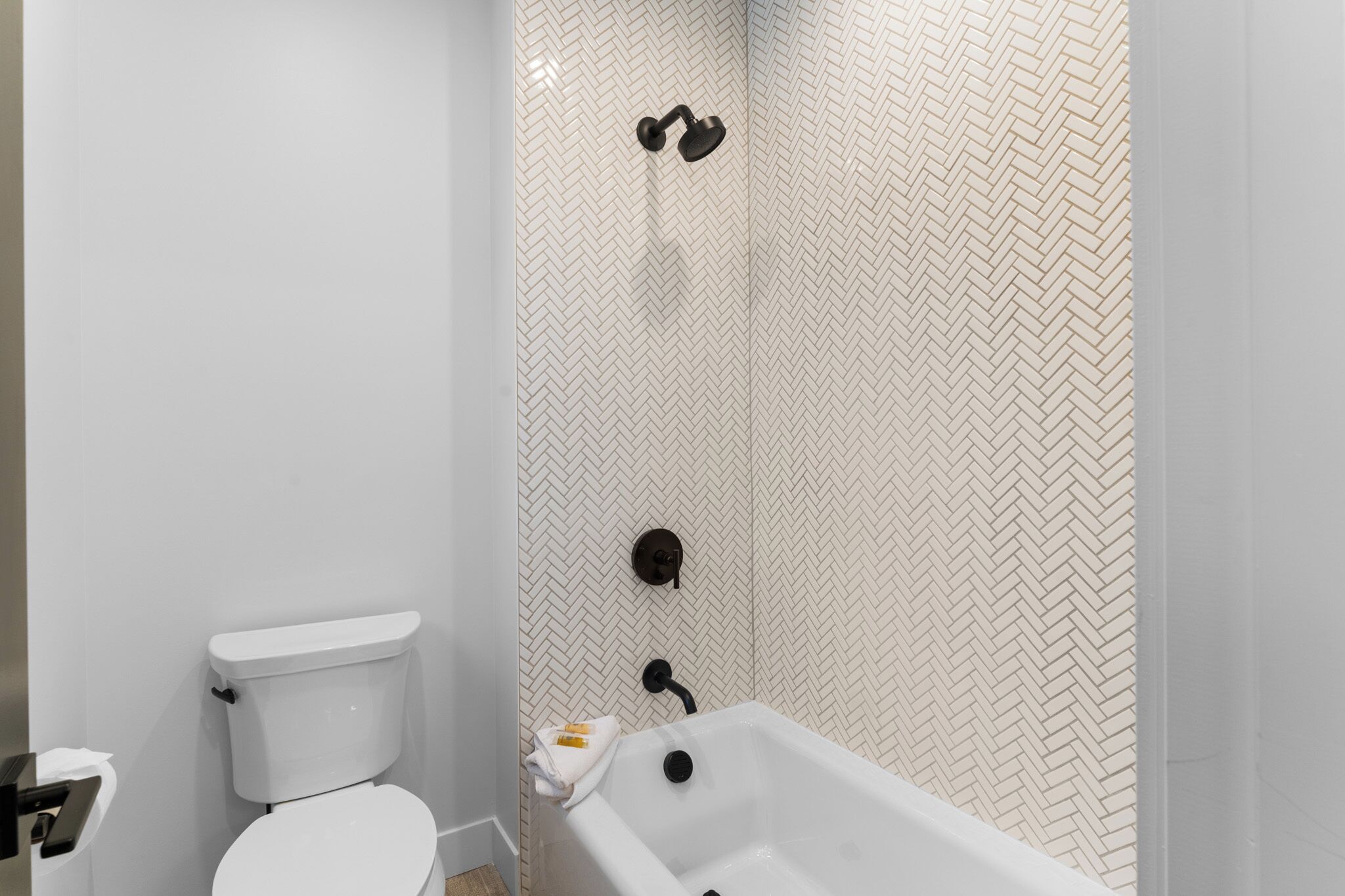 Ein Badezimmer mit Toilette, Badewanne und Dusche mit Fischgrätmuster.