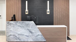 A modern reception desk with a marble top, wooden paneling, and two wall-mounted light fixtures. - Hawthorn Extended Stay by Wyndham Jackson Alpine (Alpine)
