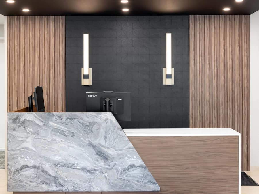 Un comptoir d’accueil moderne doté d’un plateau en marbre, de panneaux en bois et de deux luminaires fixés au mur.