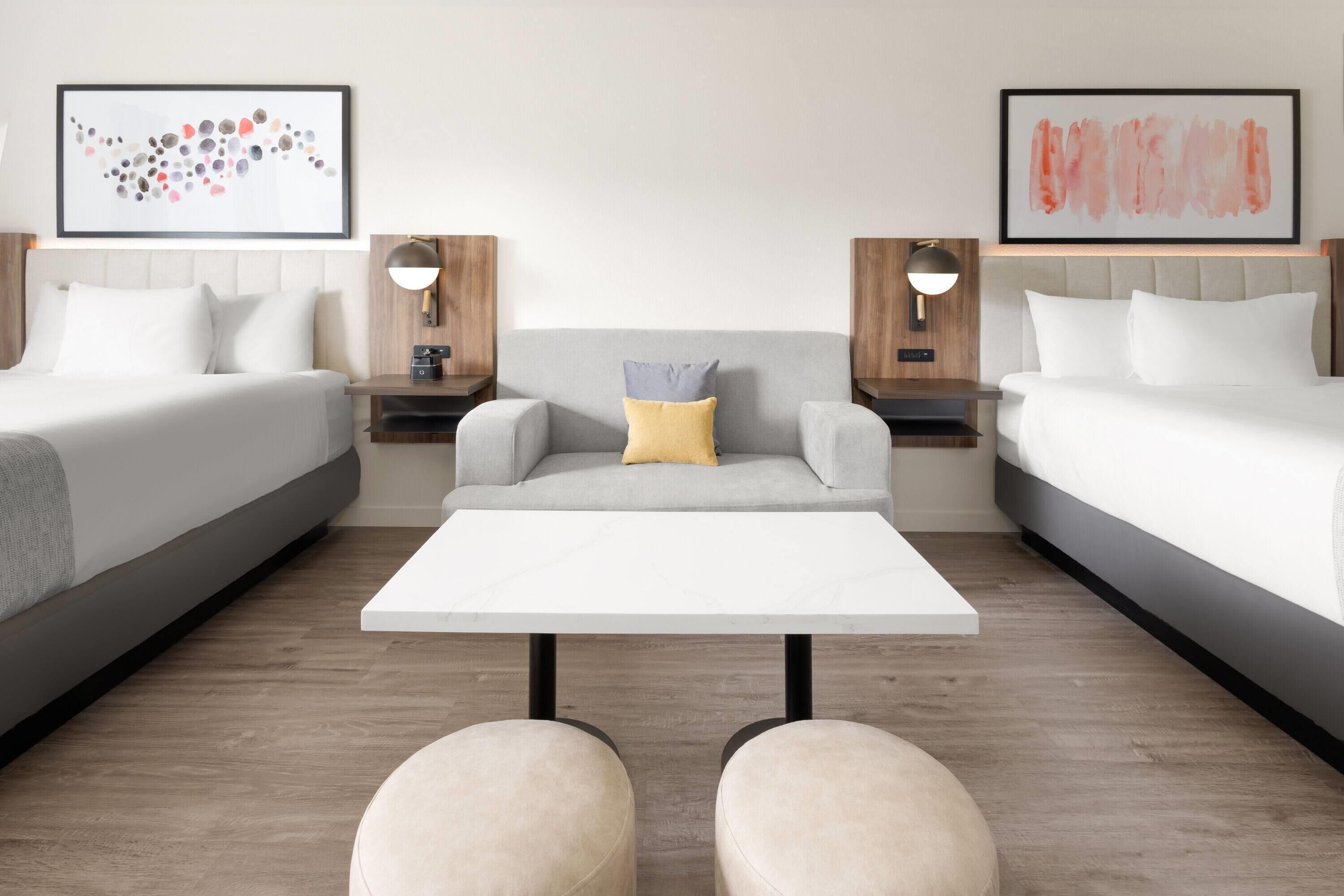 Ein Hotelzimmer mit zwei Betten, einem zentralen Sofa, einem weißen Couchtisch und zwei Nachttischen mit Lampen.
