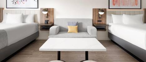 Una habitació d'hotel amb dos llits, un sofà central, una taula de cafè blanca i dues mesetes de nit amb làmpades.