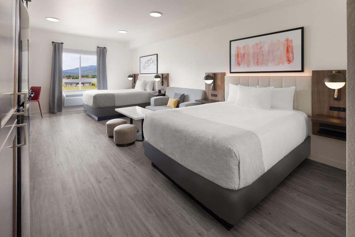 A modern hotel room with a large bed, a sofa, a desk, and a view of the outdoors.