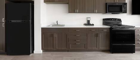 Une cuisine moderne avec des meubles de couleur bois foncé, un réfrigérateur noir, un four à micro-ondes et une cuisinière.