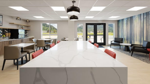 A modern meeting room with a marble island, seating, a kitchen area, and large windows offering a view of the outdoors. - Hawthorn Extended Stay by Wyndham Jackson Alpine (Alpine)