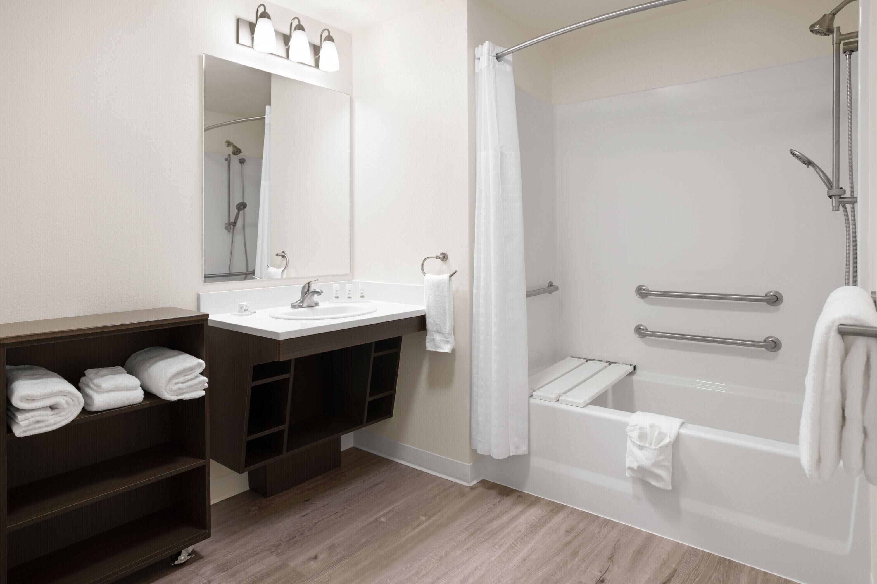 A modern bathroom with a shower, a sink, and a mirror. There are towels on a shelf and a towel rack by the shower.