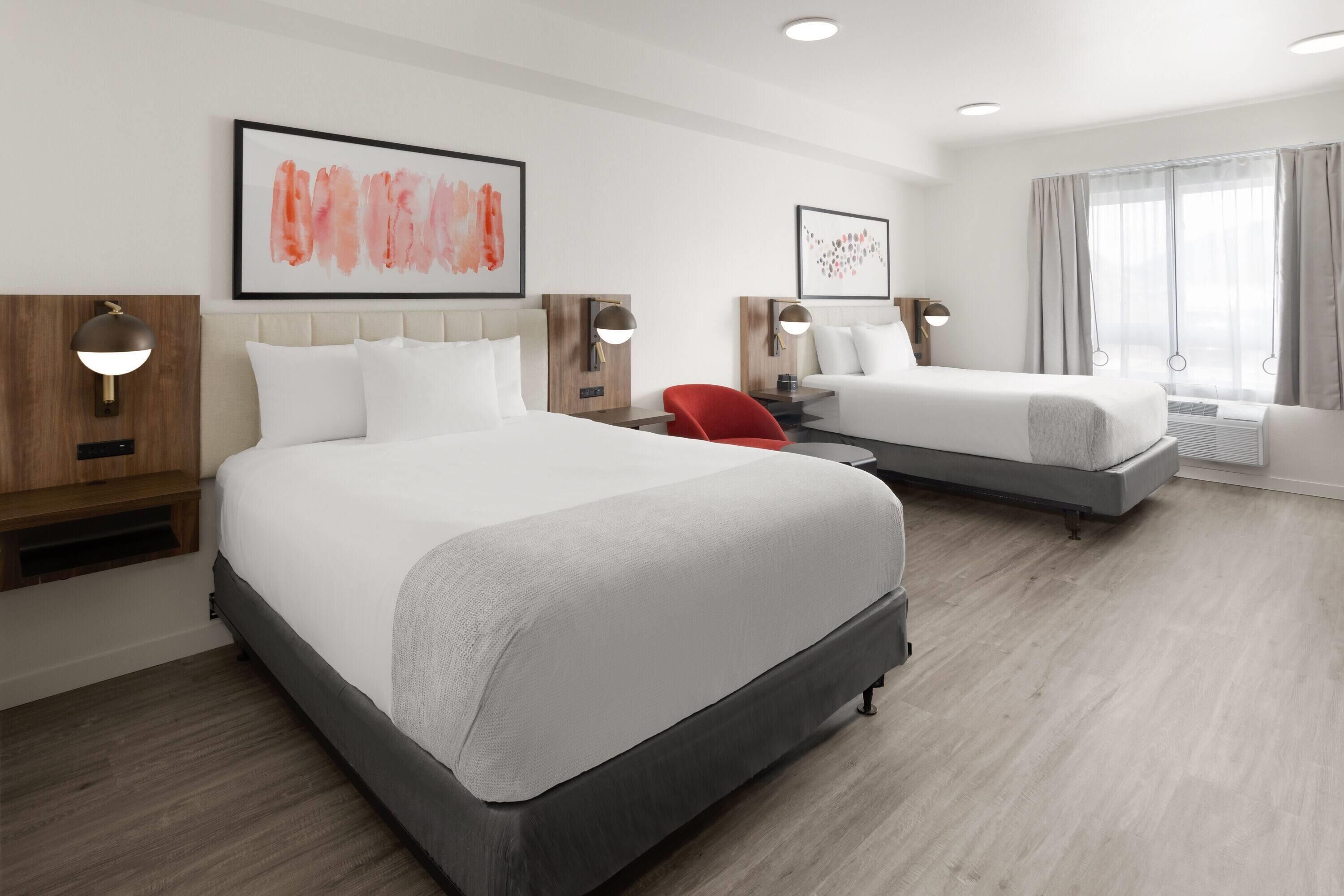 A hotel room with two beds, a red chair, and artwork on the walls.