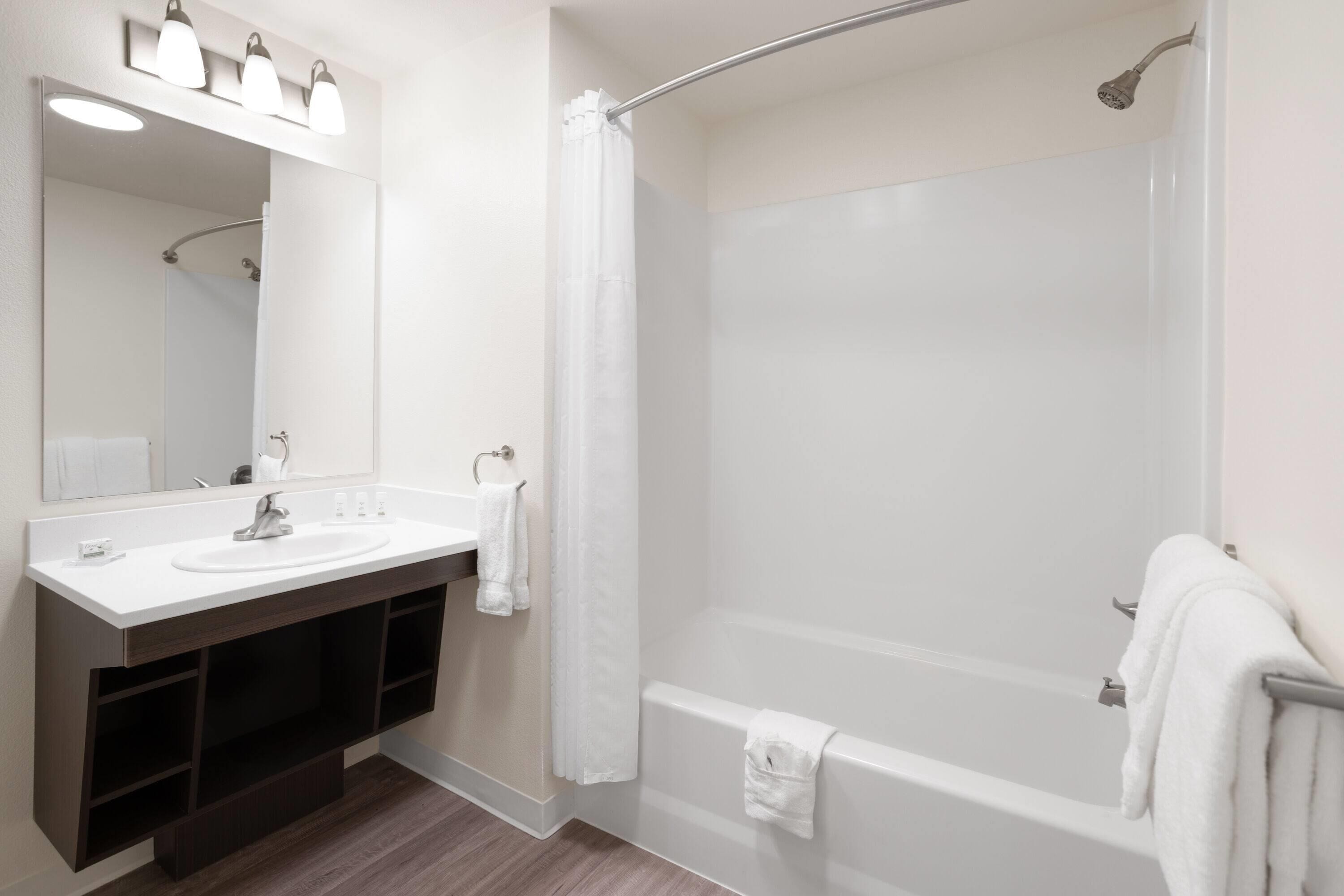 Un baño moderno con tocador doble, un espejo grande, ducha con puerta de vidrio curvada y bañera.