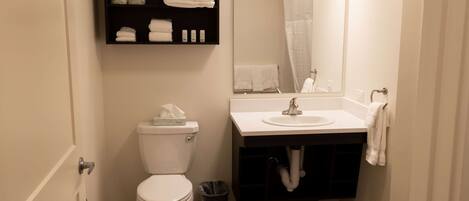 Une salle de bain équipée de toilettes, d’un lavabo, d’un miroir et d’étagères où sont rangées les serviettes.